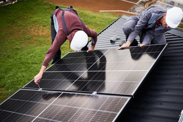 Installers installing photovoltaic solar panels on roof of house. Men engineers in helmets building solar module system with help of hex key. Concept of alternative, renewable energy.